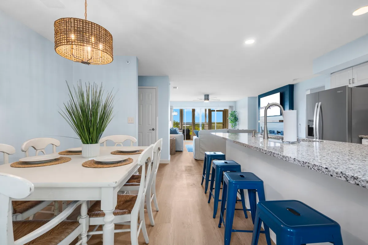 A view of the open-concept kitchen and dining area, featuring a modern dining table, a spacious kitchen island, stylish chandelier, and windows that draw in natural light. The setting is bright and cheerful, ideal for shared meals and casual gatherings.