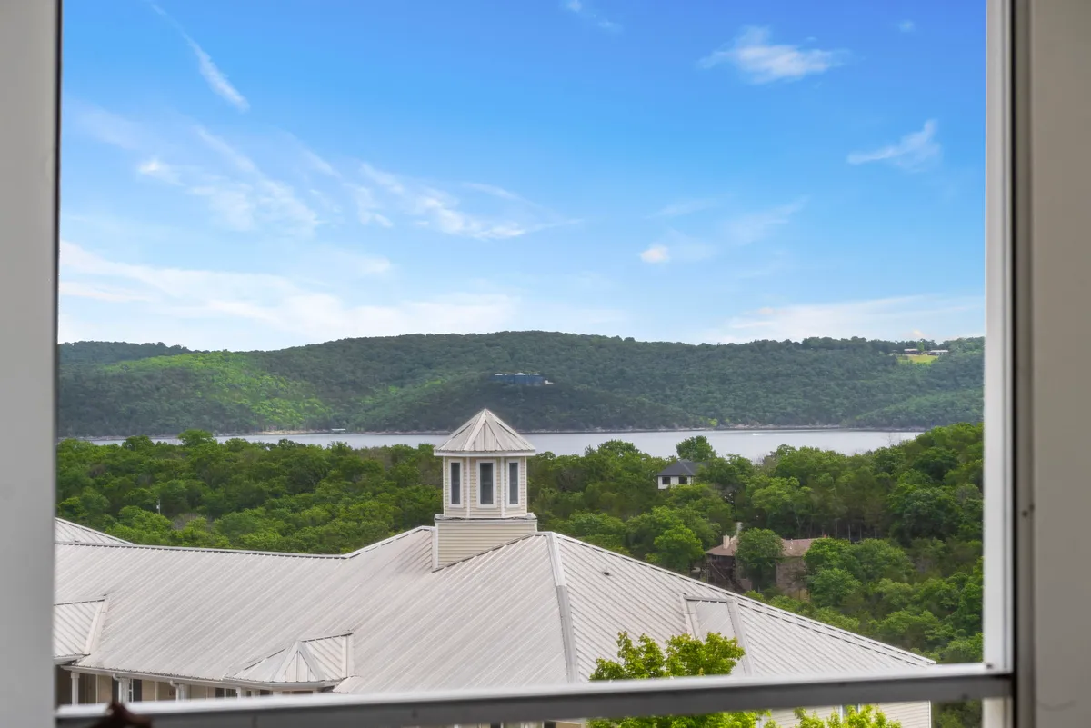 A tranquil lakeside view featuring a calm river bordered by trees and mountains, with a rooftop structure in the foreground—evoking the peaceful, romantic atmosphere of evening lakeside strolls.