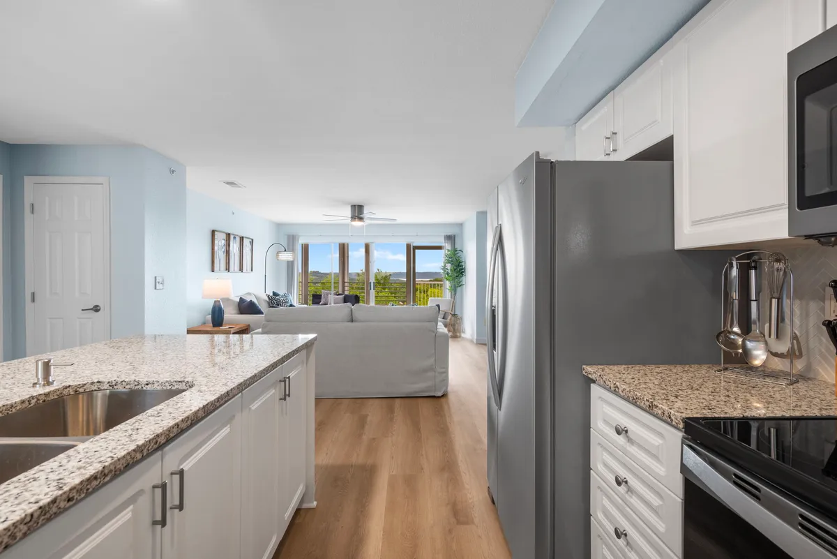 A welcoming interior scene blending the kitchen and living area, with a granite countertop, modern appliances, a sofa with cozy cushions, and expansive windows offering scenic views. The space is both functional and inviting, perfect for entertaining and relaxation.