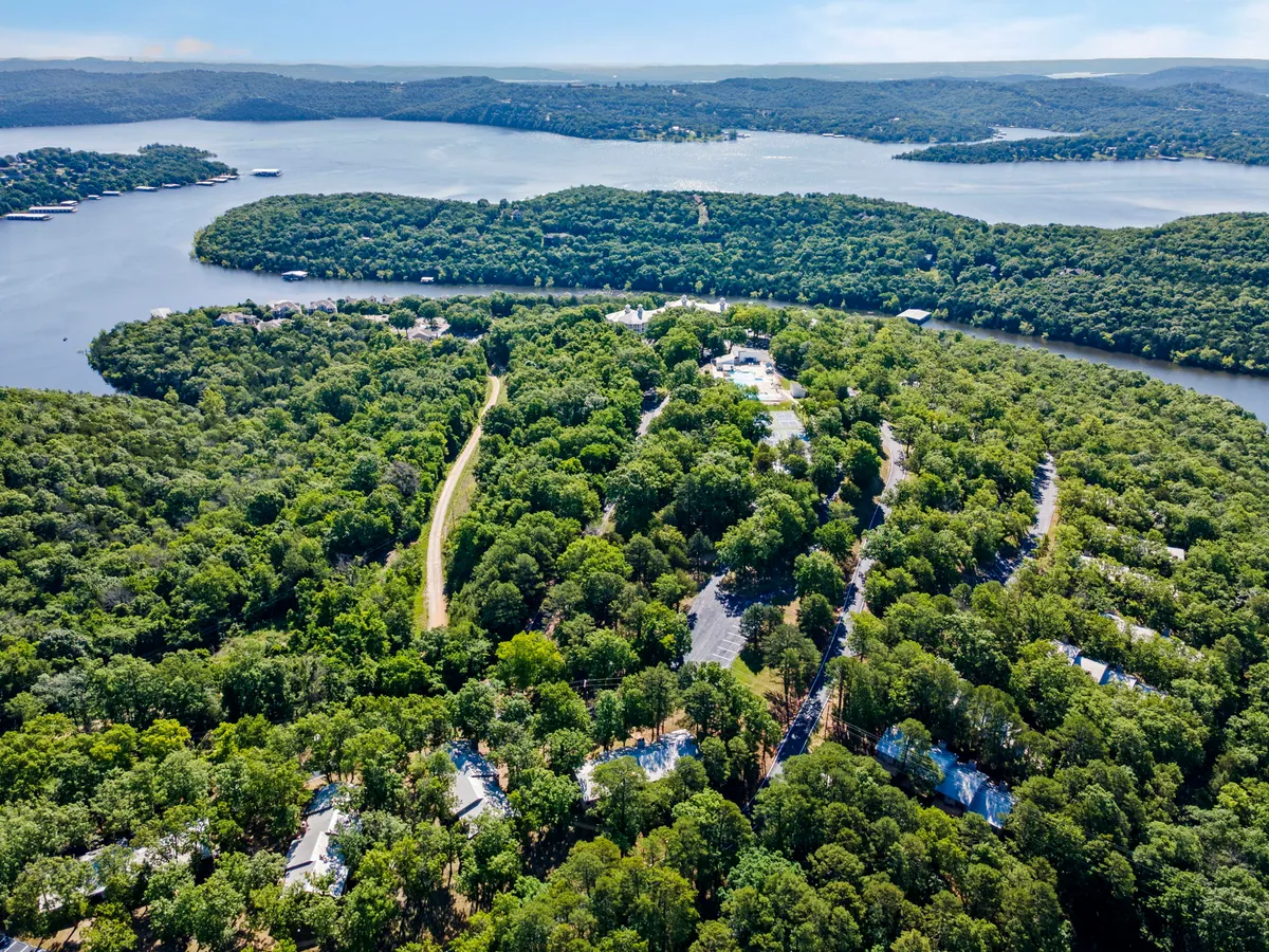 A peaceful panorama featuring lush greenery, a gently curving road, the sparkling lake, and residential buildings. The expansive view highlights the natural beauty of the area and the easy access to both water and trails for exploration.