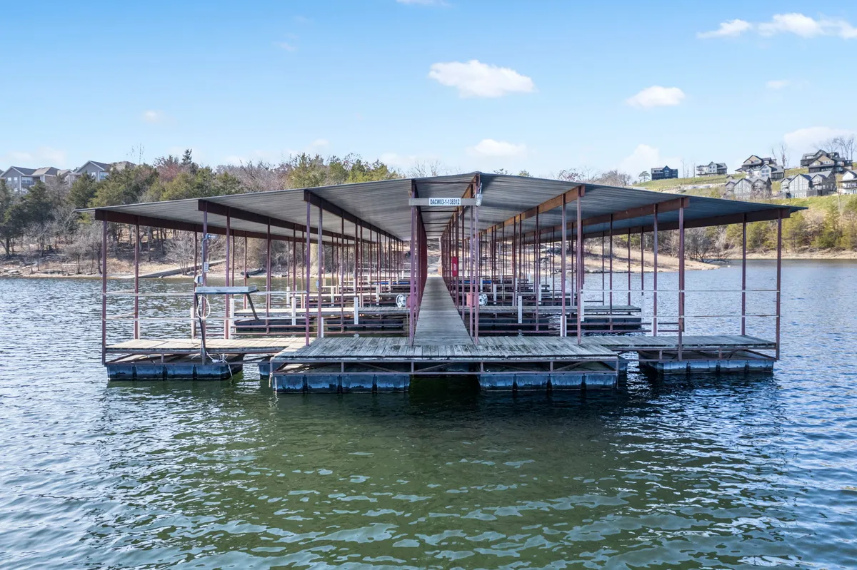 A tranquil dock juts out over calm waters, surrounded by leafy trees and distant lakeside homes. The setting sun casts a soft glow, inviting guests to imagine peaceful moments of fishing, boating, or simply unwinding by the lake.