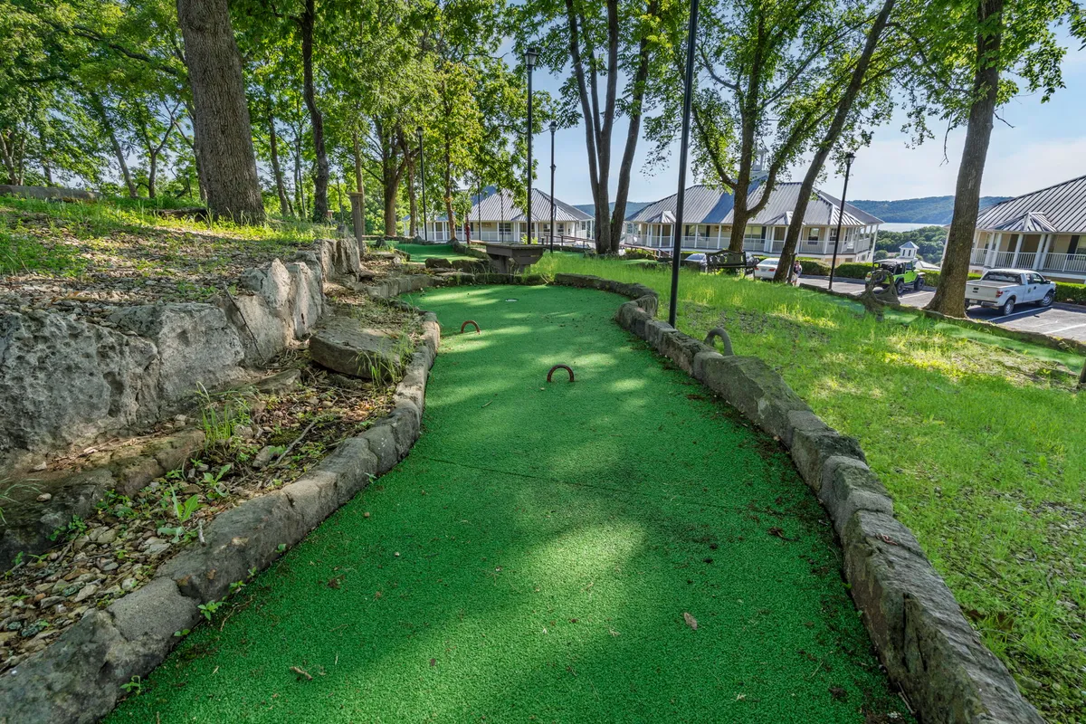 This image displays a vibrant mini-golf course surrounded by natural greenery and stone pathways. The course looks well-maintained and inviting, perfect for friendly family competition. The environment radiates a joyful, relaxed mood and is clearly designed for group enjoyment and playful interaction.