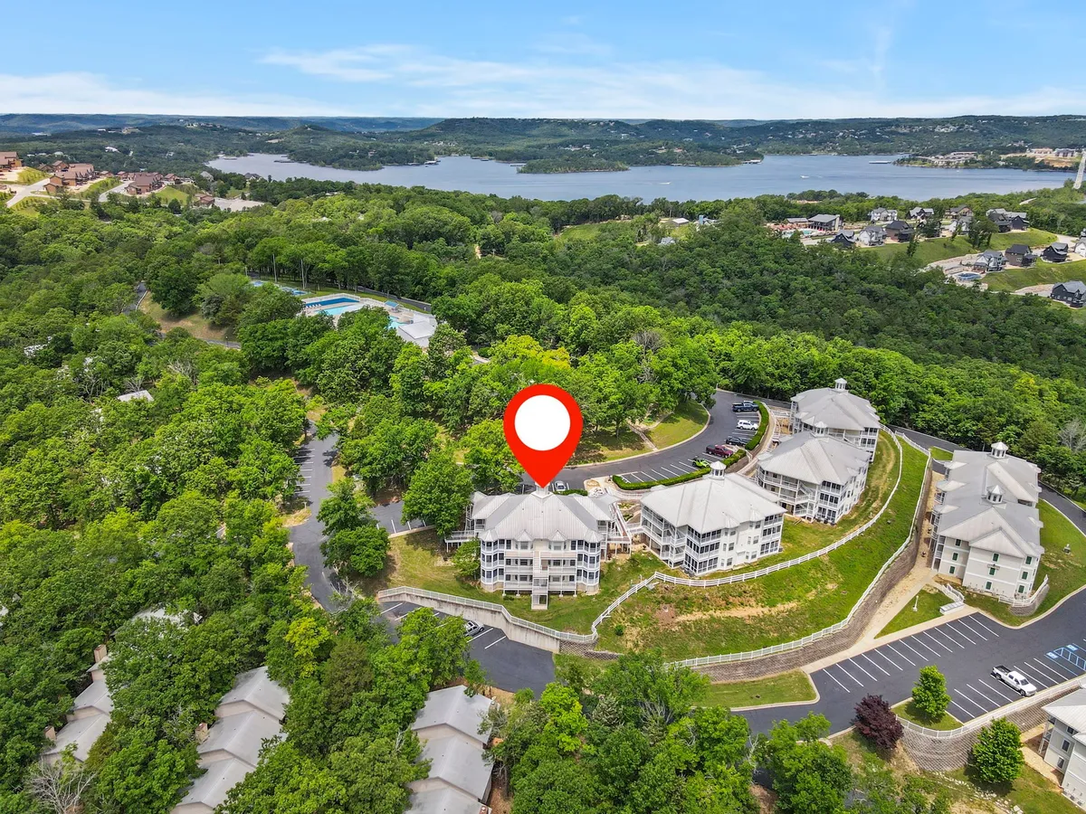 A tranquil exterior scene featuring lush greenery, a sparkling lake, a glimpse of the architectural layout of the buildings, and the inviting swimming pool. The landscaping and water views evoke a peaceful, immersive nature experience.