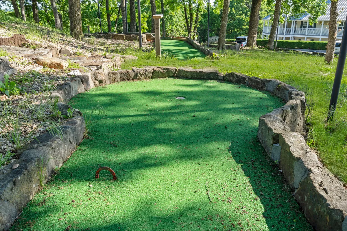 A vibrant exterior shot of the resort’s mini-golf course nestled among mature trees, with green turf, stone borders, and hints of playful activity. The natural surroundings evoke a welcoming, family-friendly vibe ideal for outdoor fun.