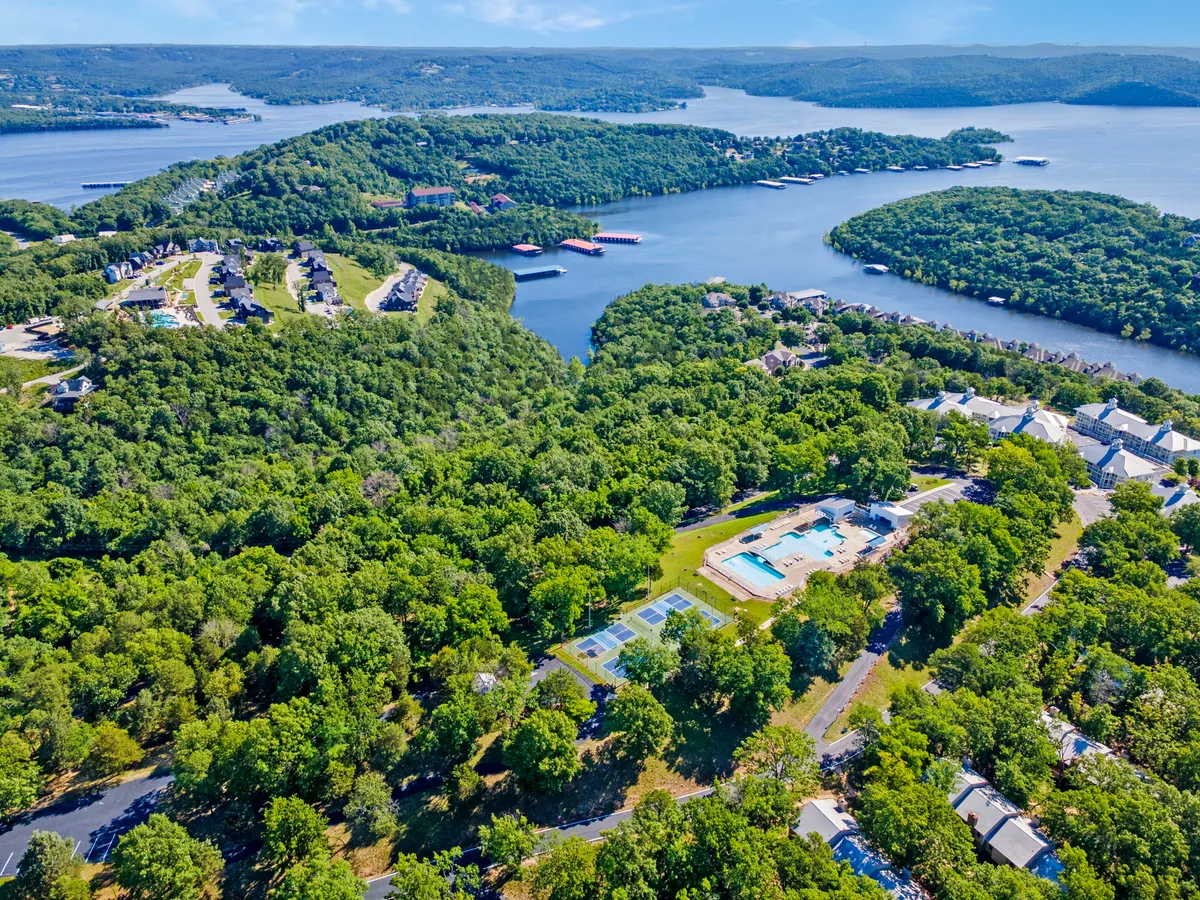 A sweeping exterior view captures the resort grounds, including the expansive lake, surrounding greenery, swimming pools, and tennis courts. The scene is bathed in soft natural light, hinting at both morning and evening possibilities for activities.