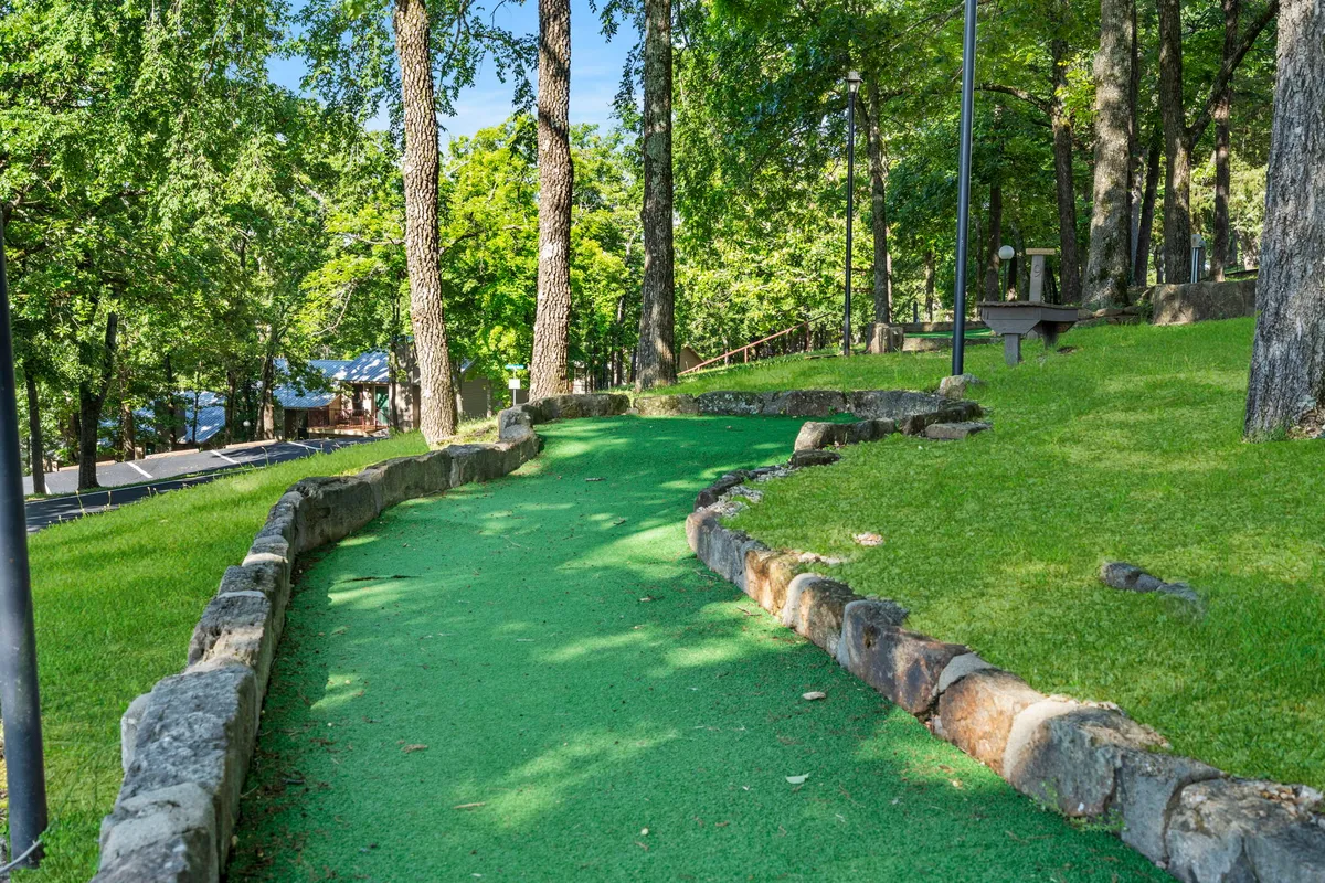 A cheerful mini-golf area with a green pathway, trees, and stone borders, inviting guests to enjoy playful competition and relaxing outdoor activities.