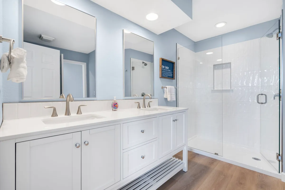 A bright and refreshing ensuite bathroom featuring a double sink vanity with expansive mirrors and a sleek glass shower enclosure. The atmosphere is calm and rejuvenating, perfect for unwinding or starting the day.