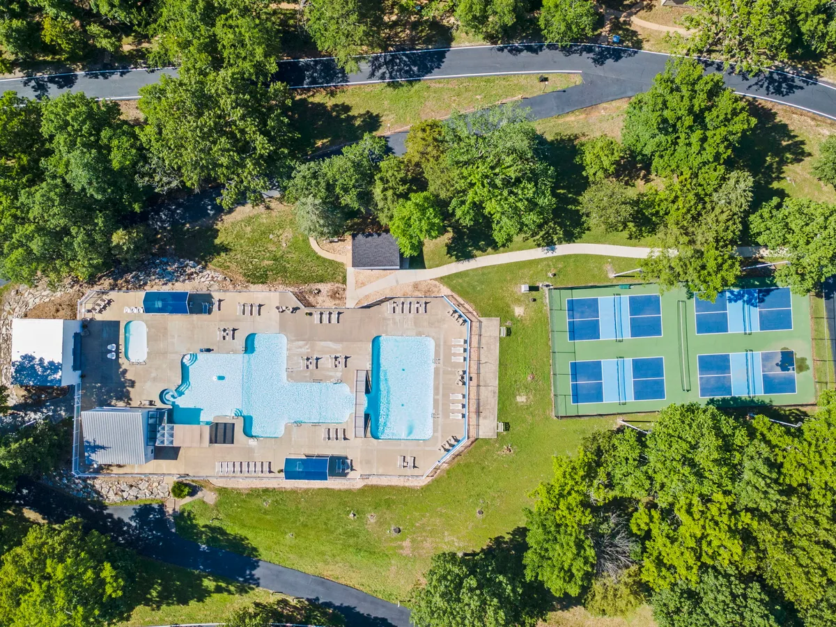 This exterior shot features both a large swimming pool and tennis courts, framed by sun loungers and vibrant greenery. The scene buzzes with the potential for active play, social gatherings, and relaxation, all in a single glance.