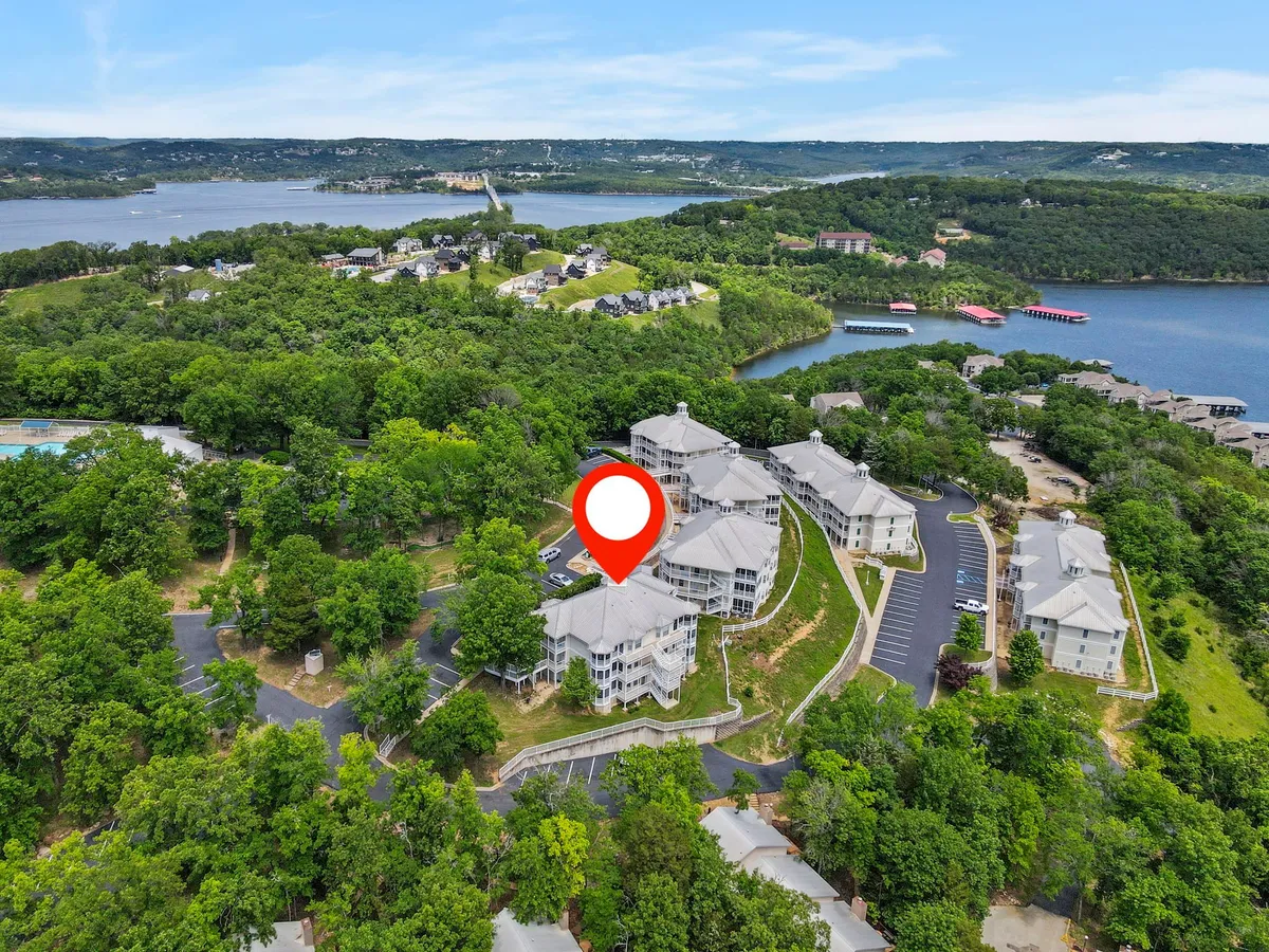A serene exterior shot featuring residential buildings nestled among a tree canopy with a clear view of the lake and roadways. The setting is peaceful and inviting, reflecting opportunities for outdoor activities like hiking and lakeside strolls.